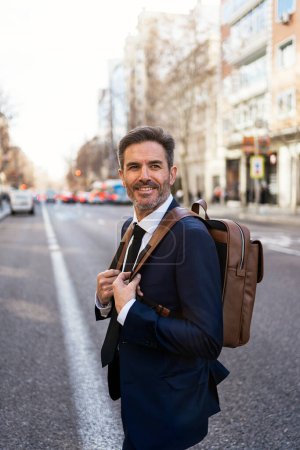 Téléchargez les photos : Portrait d'entrepreneur masculin en costume chic et avec boisson à emporter marchant dans la rue tout en se rendant au travail le matin - en image libre de droit