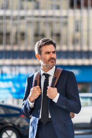 Téléchargez les photos : Portrait of male entrepreneur wearing classy suit standing with backpack in city and looking away - en image libre de droit
