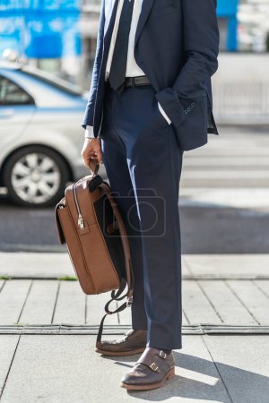 Photo for Crop anonymous male entrepreneur wearing elegant suit standing with leather backpack and hand in pocket in city on sunny day - Royalty Free Image