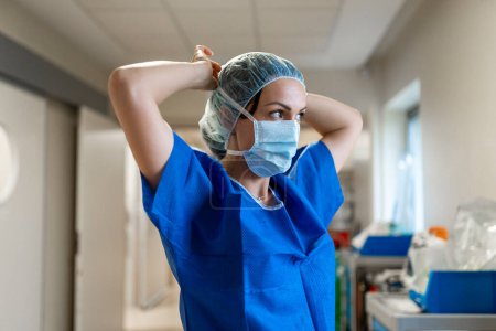 Téléchargez les photos : Nurse standing distracted while putting on her face mask in a hospital - en image libre de droit