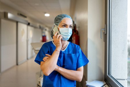 Téléchargez les photos : Female doctor with mask and cap talking to the mobile phone in a hospital ward - en image libre de droit