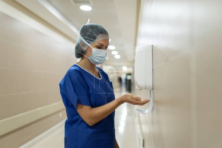 Téléchargez les photos : A female doctor putting sterilizing gel on her hands in a hospital corridor - en image libre de droit