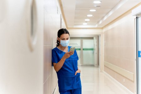 Photo for Beauty Doctor wearing mask using a mobile in a break from work - Royalty Free Image