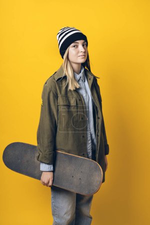 Photo for Stock photo of young expressive girl looking at camera in studio. She is holding a skateboard. - Royalty Free Image