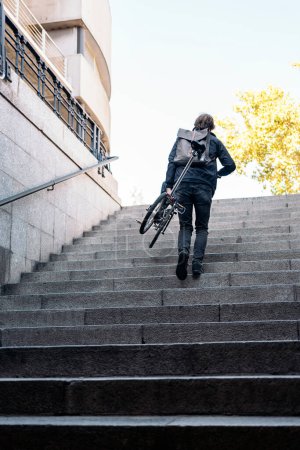 Foto de Foto en stock de un hombre no reconocido subiendo las escaleras con su bicicleta. - Imagen libre de derechos