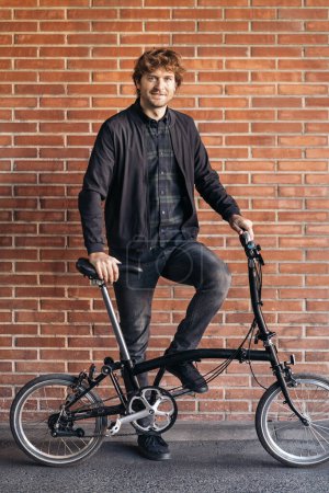 Foto de Foto de stock de hombre guapo de pie y mirando a la cámara junto a su bicicleta desmontable. - Imagen libre de derechos