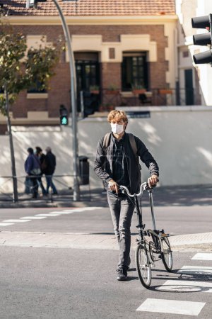 Téléchargez les photos : Stock photo of handsome man wearing face mask using his detachable bike in the street. - en image libre de droit