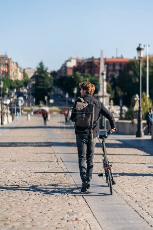 Téléchargez les photos : Photo d'un homme non reconnu utilisant son smartphone dans la rue et portant son vélo amovible. - en image libre de droit