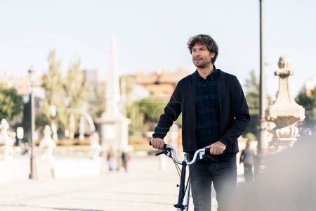 Photo for Stock photo of handsome man walking in the street carrying his detachable bike. - Royalty Free Image