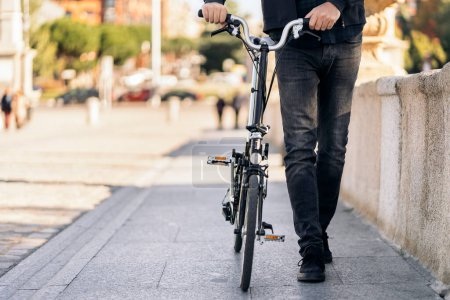 Photo for Stock photo of faceless man walking in the street next to his removable bike. - Royalty Free Image