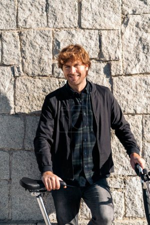 Photo for Stock photo of handsome man standing and looking at camera next to his detachable bike. - Royalty Free Image