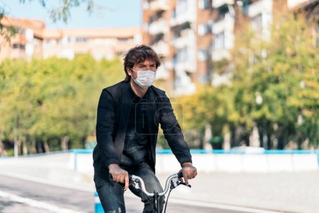 Téléchargez les photos : Photo de stock de bel homme portant un masque facial à l'aide de son vélo détachable dans la rue. - en image libre de droit