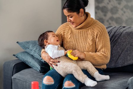 Photo for Stock photo of smiley woman holding her little baby while sitting in the sofa. - Royalty Free Image