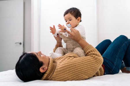 Téléchargez les photos : Photo de stock de jeune mère partageant un moment mignon avec son petit bébé couché dans le lit. - en image libre de droit