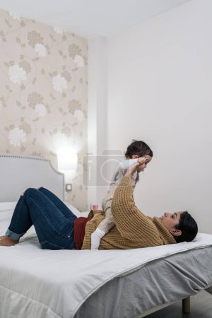 Foto de Foto de la madre joven compartiendo lindo momento con su pequeño bebé acostado en la cama. - Imagen libre de derechos