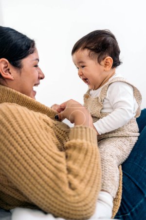 Téléchargez les photos : Photo de stock de jeune mère partageant un moment mignon avec son petit bébé dans le salon. - en image libre de droit