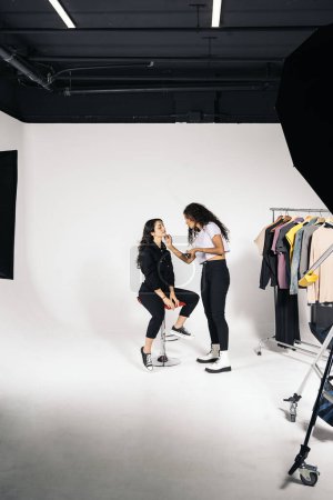 Téléchargez les photos : Stock photo of young woman applying make up to her client in studio over white background. - en image libre de droit
