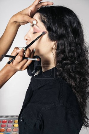 Photo for Stock photo of young make up artist doing makeup to pretty model in studio. - Royalty Free Image