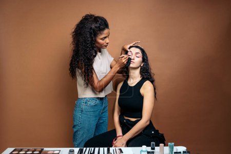 Foto de Foto de stock de maquilladora genial haciendo maquillaje a su cliente en el estudio. Ella está haciendo su delineador de ojos. - Imagen libre de derechos