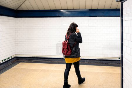 Téléchargez les photos : Stock photo of unrecognized woman talking on the phone while walking in metro station. - en image libre de droit