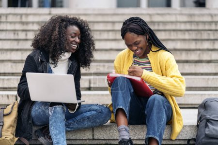 Téléchargez les photos : Stock photo of black friends using laptop while sitting in stairs and doing homework. - en image libre de droit