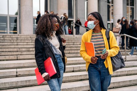 Foto de Foto de estudiantes negros hablando después de clase en la universidad. Están usando mascarilla facial debido a covid19. - Imagen libre de derechos