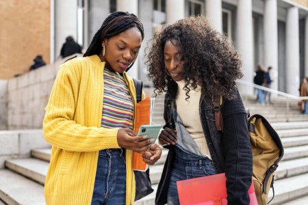 Photo for Stock photo of black female students talking and using phone outside the college campus. - Royalty Free Image