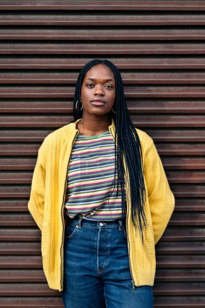 Téléchargez les photos : Stock photo of serious young black girl looking at camera and standing against wall. - en image libre de droit