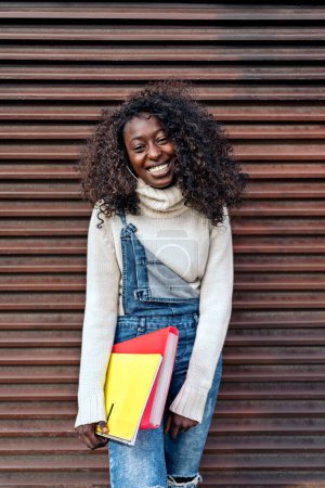 Téléchargez les photos : Stock photo of young black girl holding notebook, smiling and looking at camera. - en image libre de droit