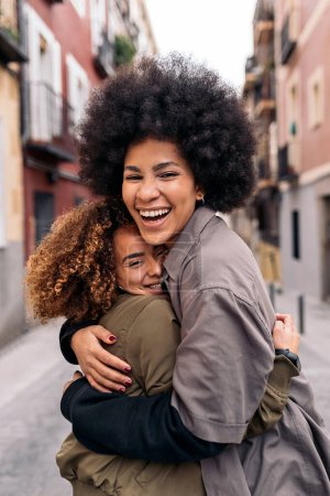 Foto de Foto de stock de chicas afro encantadoras abrazándose en la calle y mirando a la cámara. - Imagen libre de derechos