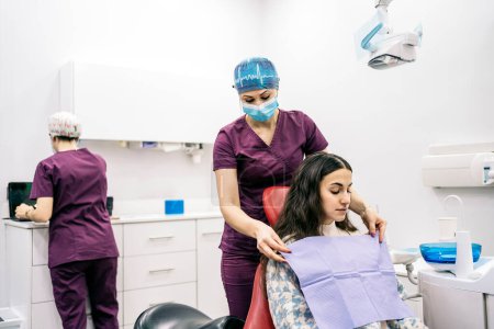 Téléchargez les photos : Photo de stock de dentiste féminine portant un masque facial préparant la fille pour son check-up. - en image libre de droit