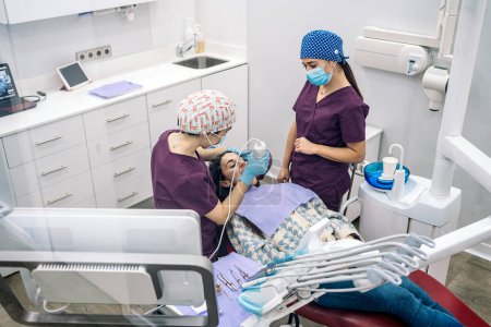 Téléchargez les photos : Stock photo of unrecognized female dentists wearing latex gloves examining a patient. - en image libre de droit