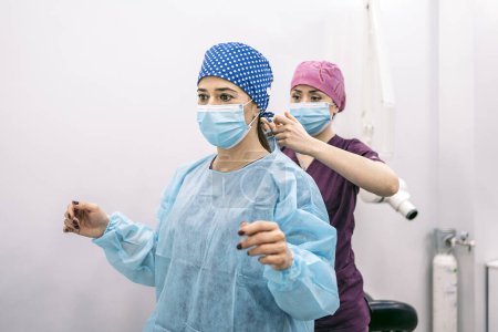 Photo pour Stock photo of woman wearing face mask and hair net helping her coworker in a dental clinic. - image libre de droit