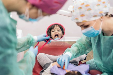 Téléchargez les photos : Photo de stock de la jeune fille dans la clinique dentaire apprendre à nettoyer ses dents avec un miroir. - en image libre de droit
