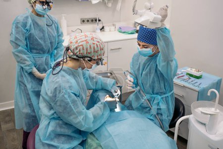 Téléchargez les photos : Photo de l'équipe de femmes portant des masques faciaux et des filets à cheveux travaillant dans une clinique dentaire. - en image libre de droit