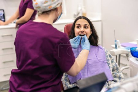 Foto de Stock photo of woman sitting in dentist's chair putting on teeth covers. - Imagen libre de derechos