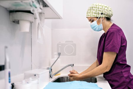 Téléchargez les photos : Stock photo of woman wearing face mask and hair net working in modern dental clinic washing her hands. - en image libre de droit