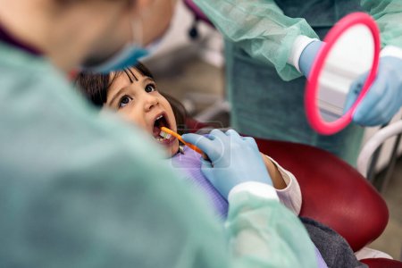 Téléchargez les photos : Stock photo of unrecognized professional dental workers wearing face mask due to covid19 doing cleaning treatment to a young girl. - en image libre de droit
