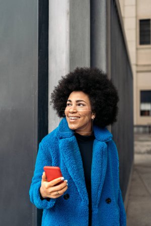 Téléchargez les photos : Photo de stock de belle fille afro-américaine souriant et utilisant le téléphone mobile dans la ville. - en image libre de droit
