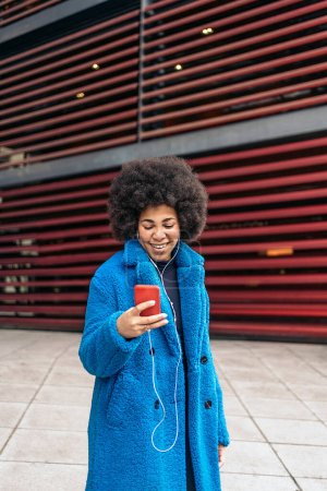 Téléchargez les photos : Photo de stock de belle fille afro-américaine utilisant un téléphone mobile et portant des écouteurs. - en image libre de droit