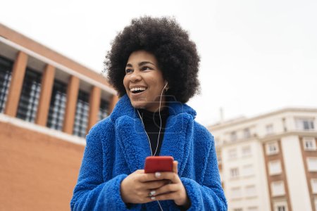Foto de Foto de stock de hermosa chica afroamericana sonriendo y utilizando el teléfono móvil en la ciudad. - Imagen libre de derechos