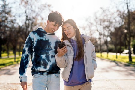 Photo for Stock photo of happy friends talking and using phone while walking in the park. - Royalty Free Image