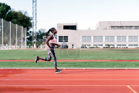 Téléchargez les photos : Photo d'une vue de côté d'un sprinteur afro-américain courant sur une piste d'athlétisme - en image libre de droit