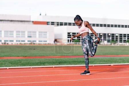 Téléchargez les photos : Photo en stock d'une sprinteuse afro-américaine étirant ses jambes avant de s'entraîner - en image libre de droit