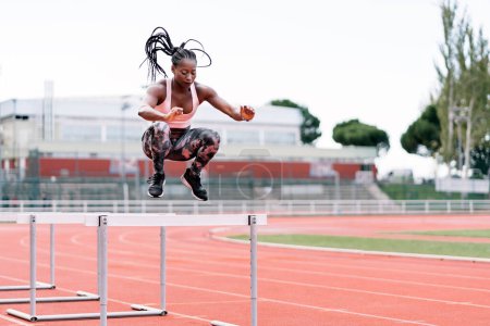 Téléchargez les photos : Photo d'un sprinteur afro-américain sautant un obstacle dans le centre sportif - en image libre de droit