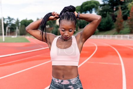 Photo for Stock photo of an African-American sprinter standing on an athletics track touching her braided hair with her hand. Sports - Royalty Free Image