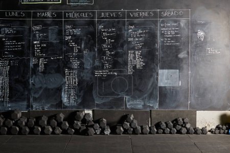Photo for Stock photo of a workout plan written with chalk on a blackboard with a lot of weights underneath it. There are nobody on the picture. - Royalty Free Image