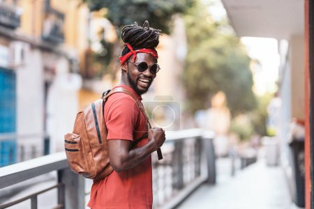 Téléchargez les photos : Photo de stock de heureux garçon afro-américain avec dreadlocks et un bandana marchant dans la rue. - en image libre de droit