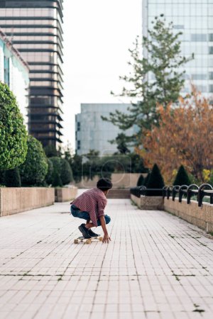 Téléchargez les photos : Photo de stock de garçon afro non reconnu faisant du skate dans le parc avec son longboard. - en image libre de droit