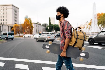 Téléchargez les photos : Photo de stock de jeune garçon afro portant un masque facial en raison de la marche covid19 dans la ville. - en image libre de droit